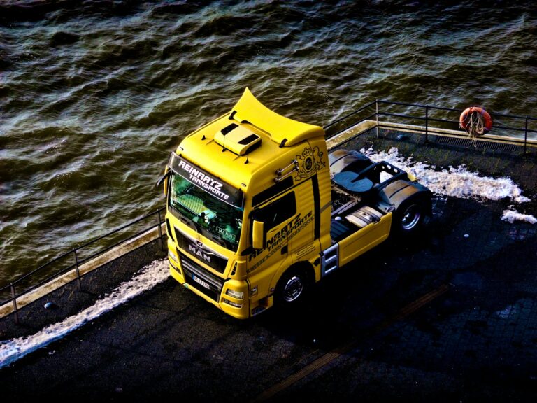 a yellow truck driving down a street next to a body of water